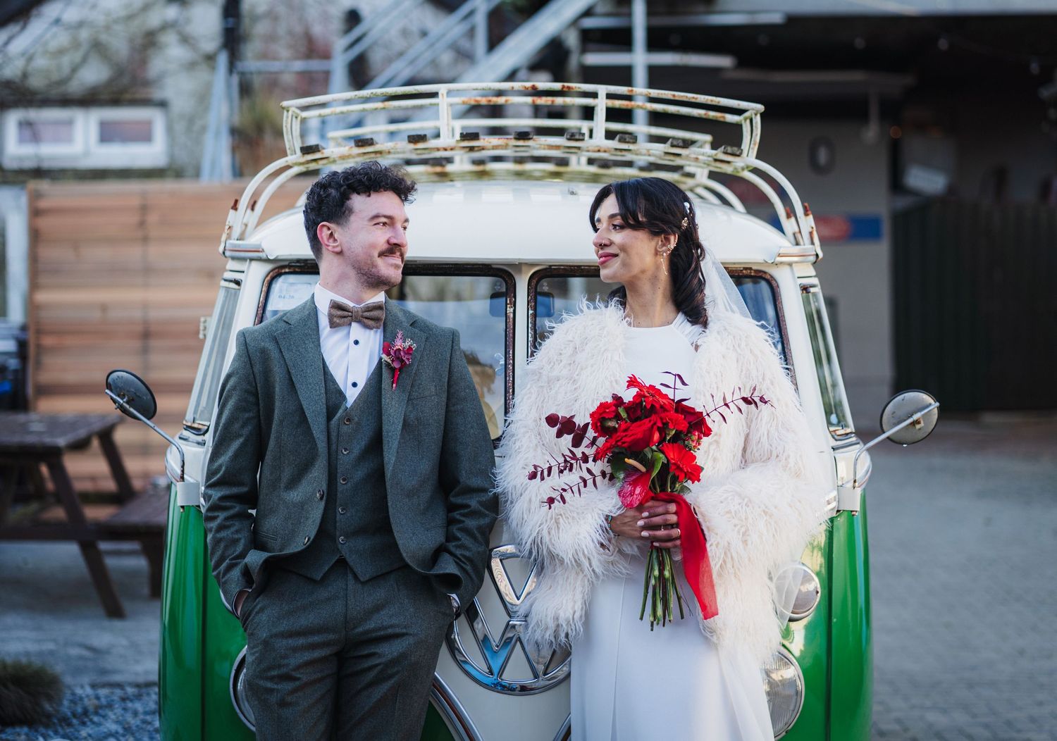 A wedding couple poses with a vintage green and white Volkswagen bus decorated for their special day.