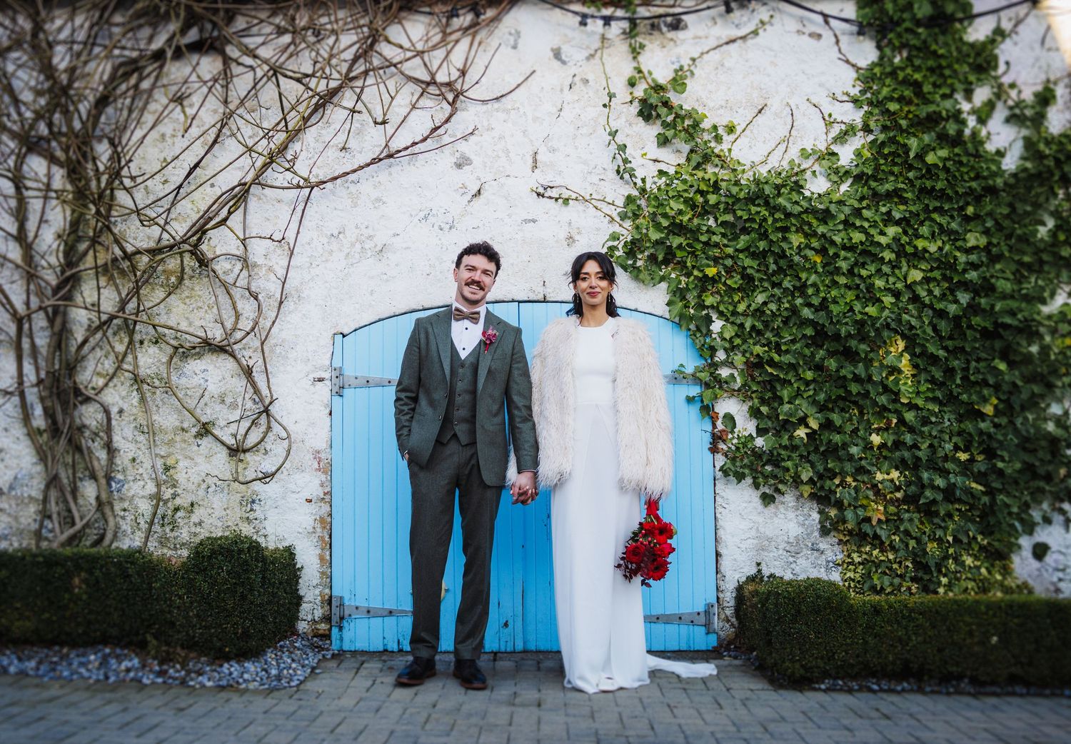 A panoramic sequence of wedding photos showing a couple posing against a rustic wall with blue doors and ivy.