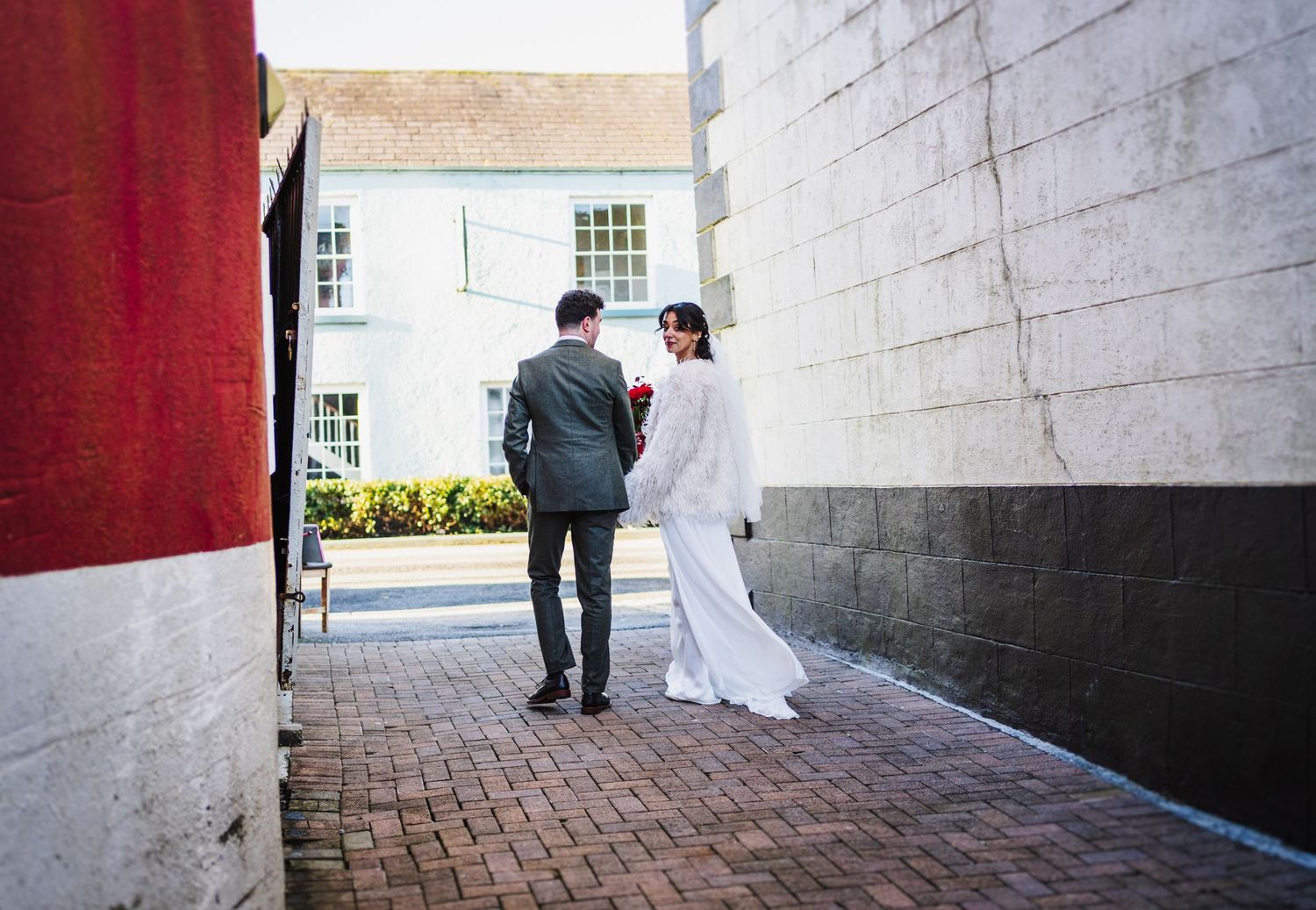 A series of connected wedding photos showing a couple walking along a brick path next to a white stone wall.