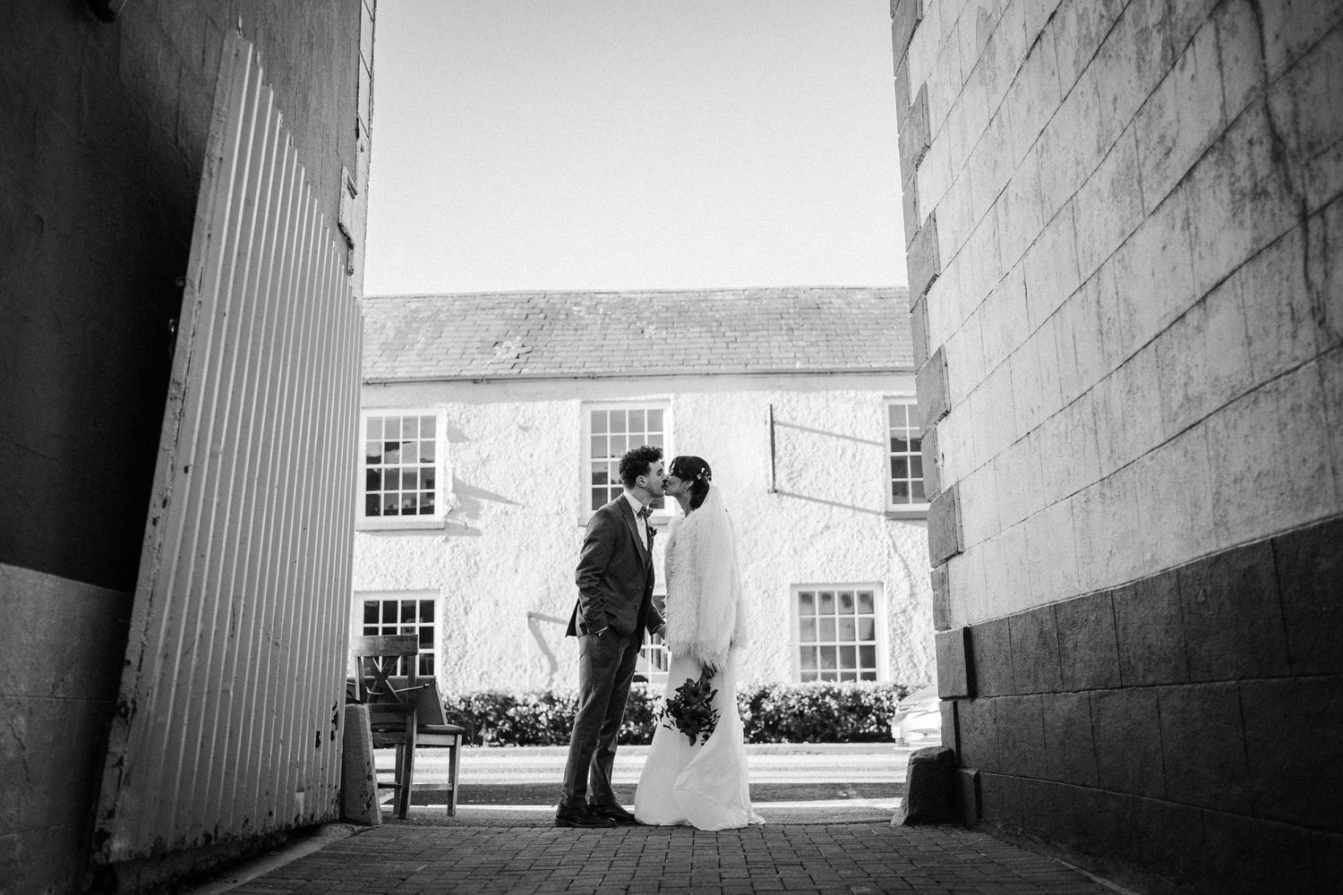 A black and white photo shows a couple standing in a dramatic architectural corridor with tall columns and shadows.