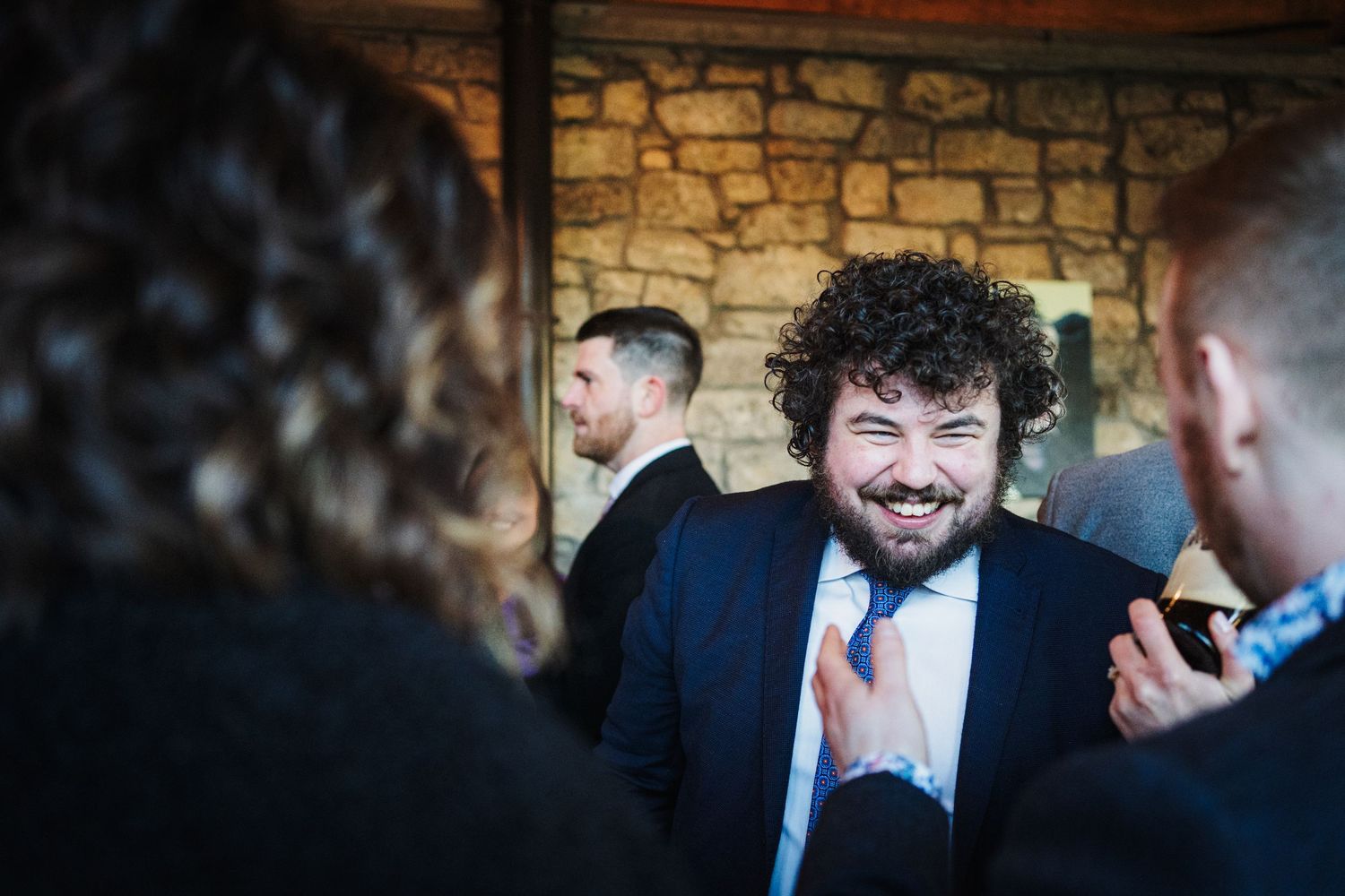 A joyful moment captured at a wedding reception with guests laughing together against a rustic stone wall background.