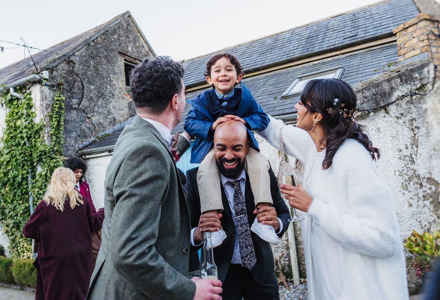 A joyful group shares a laugh together during an outdoor gathering near a stone building.