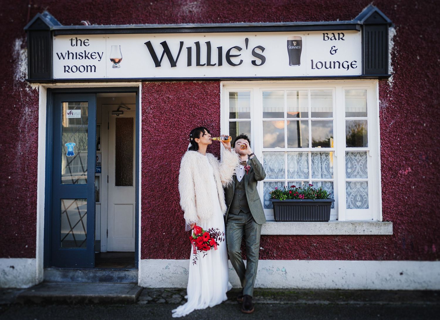 Wedding couple poses outside Willie's pub with burgundy exterior and white trim windows.