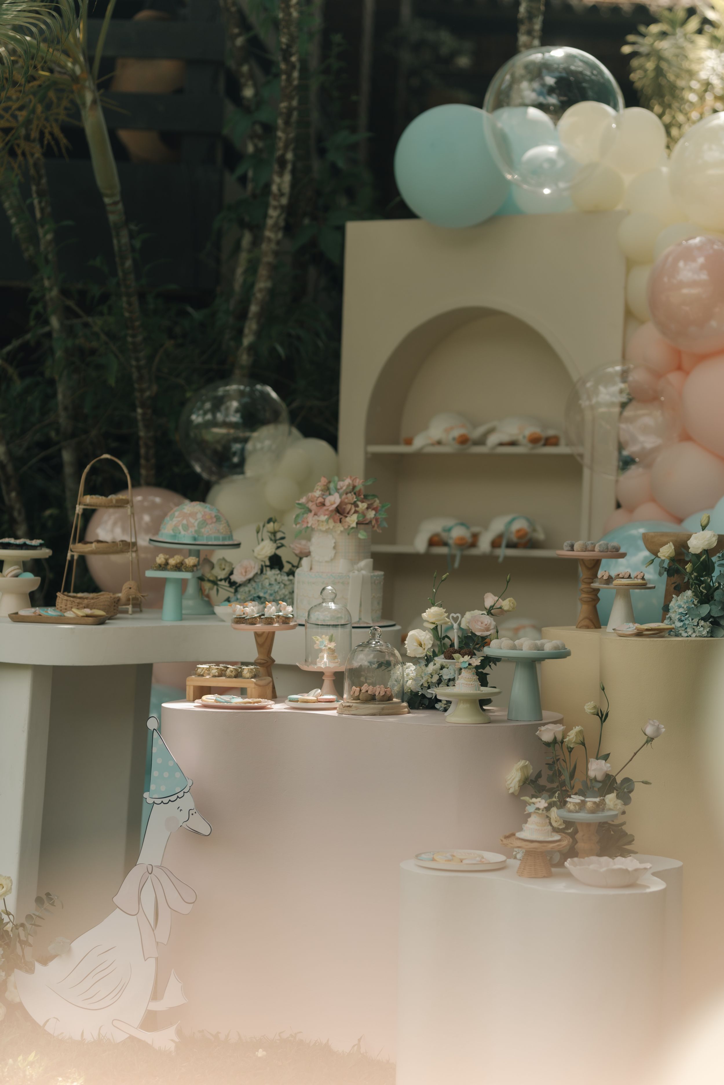 Elegant dessert table setup with pastel blue and pink balloons, tiered displays, and delicate decorations for a party.