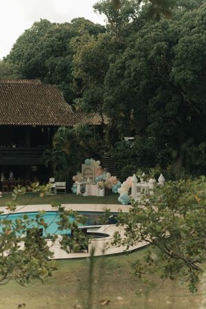 Swimming pool surrounded by lush green trees and a rustic building in a tranquil outdoor setting.