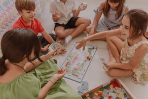 Children sitting on floor playing board games and cards together during party activities.