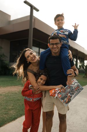 Happy family poses outdoors together wearing casual clothes and racing-themed outfits on a sunny day.