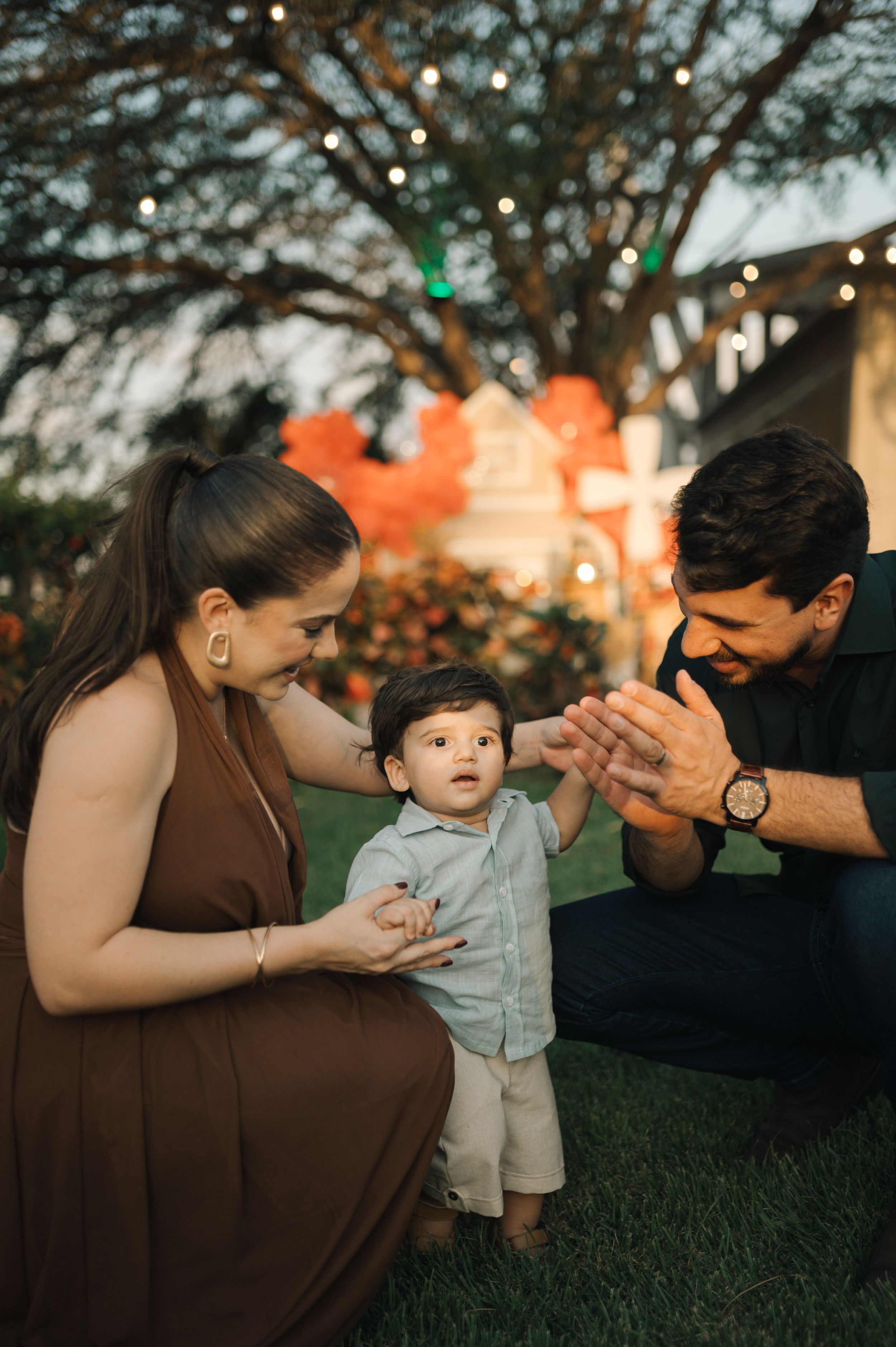Family shares tender outdoor moment at sunset with string lights glowing in background.