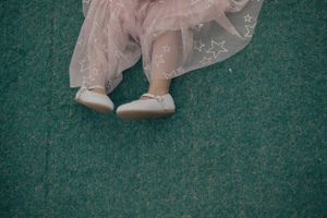 Small white dress shoes and tulle skirt hem visible against green carpet background.