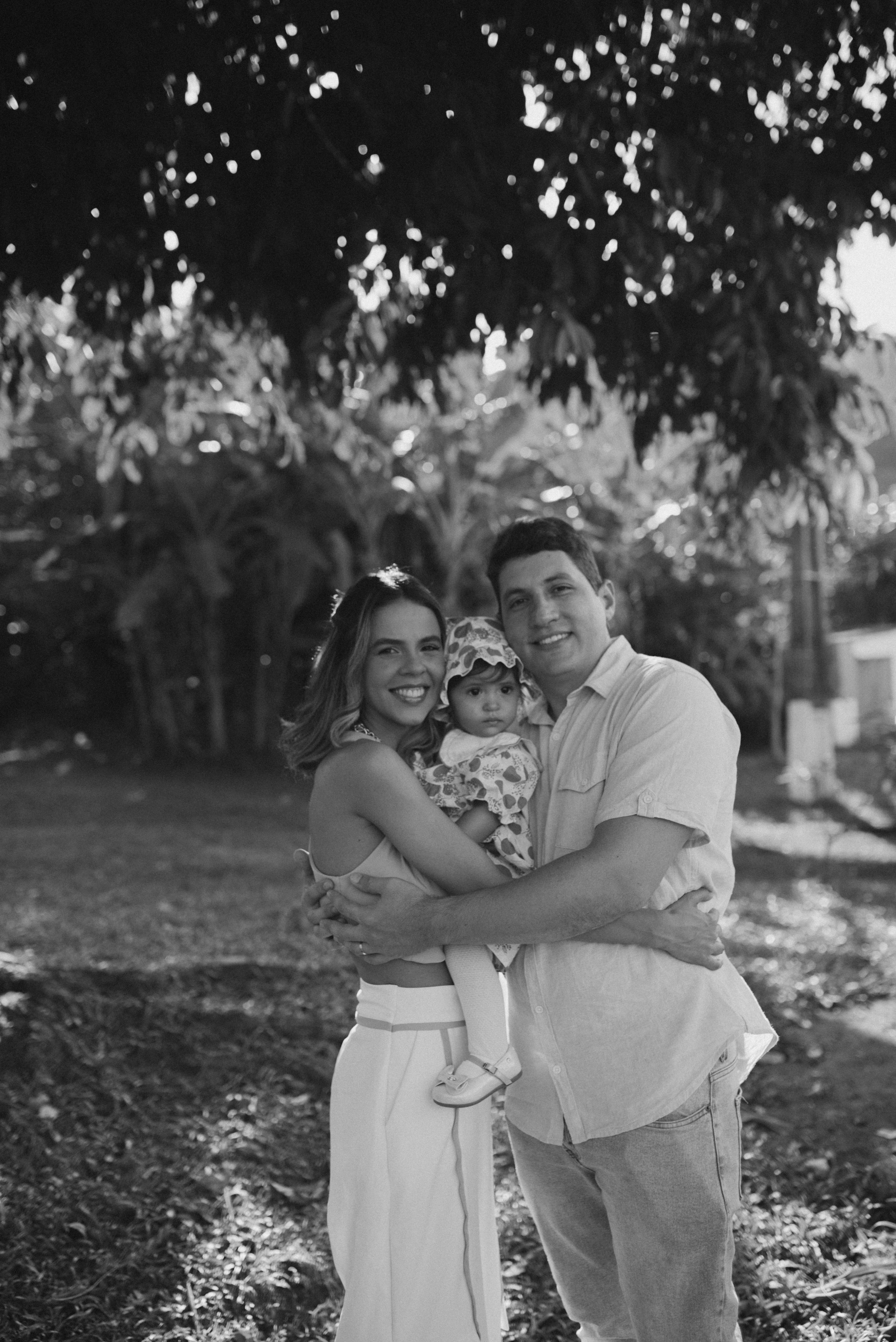 A black and white outdoor family portrait taken under leafy trees.
