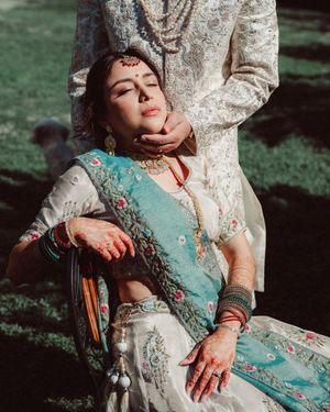 Person in turquoise and white lace dress poses elegantly on antique chair in dramatic sunlit outdoor setting.