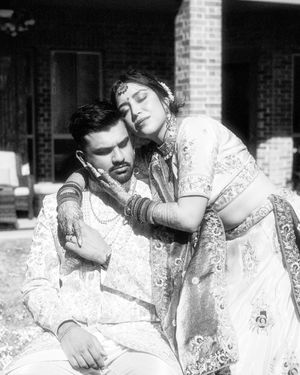 A vintage black and white photograph showing a romantic scene with two people in traditional Indian attire outdoors.