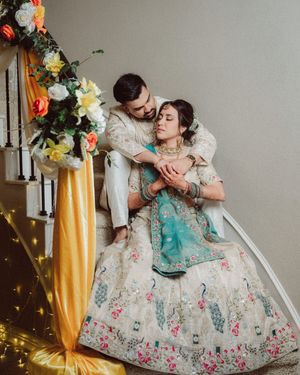 A couple in ornate vintage-style attire share romantic poses against a backdrop with gold curtains and twinkling lights.
