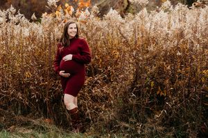 A person in a burgundy dress poses gracefully in a golden autumn field during sunset.