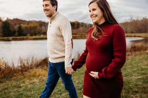 A couple walks together in a fall field by a lake, wearing cozy sweaters as they share a joyful moment outdoors.