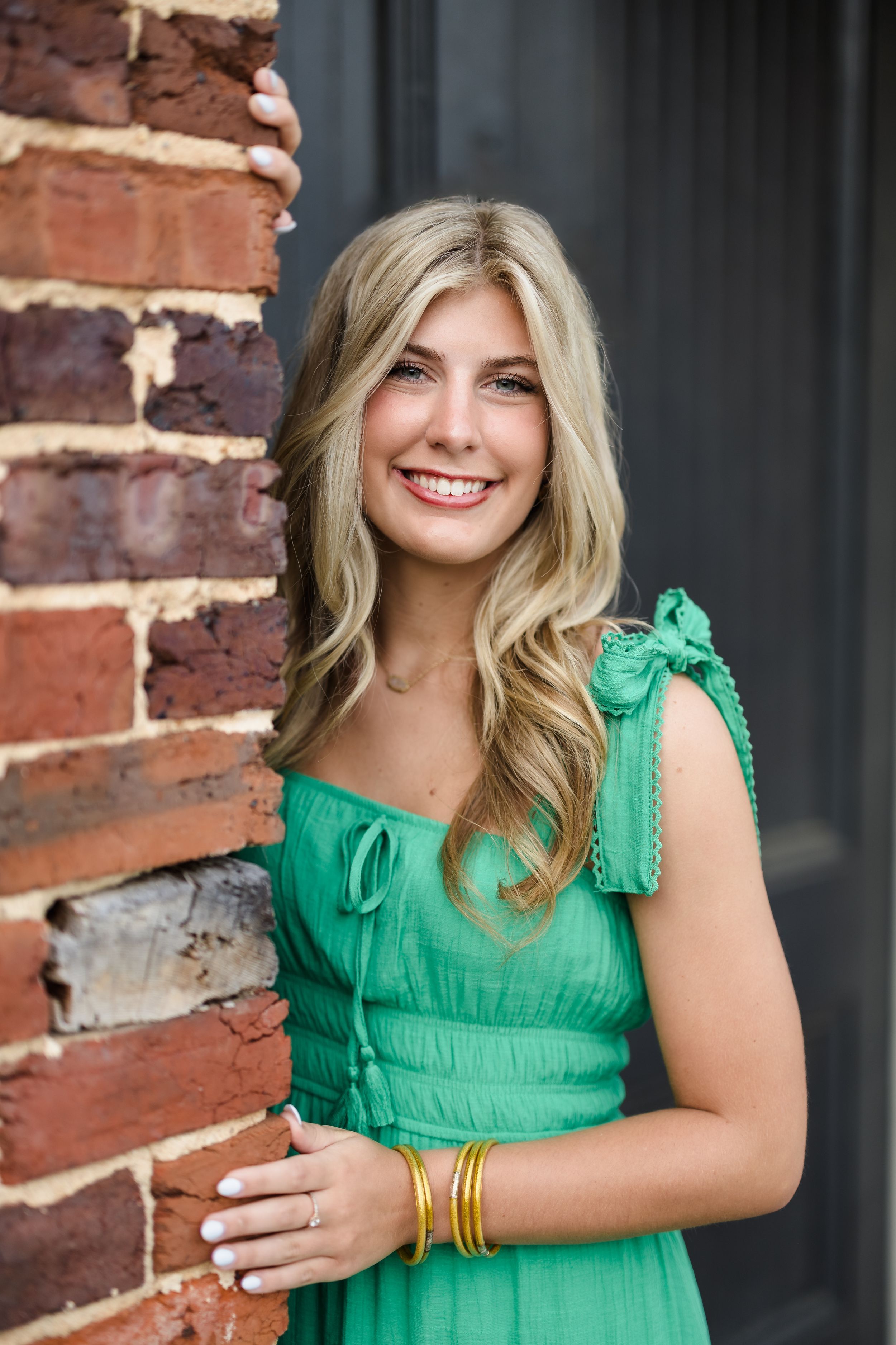 A vibrant green dress is worn in a photoshoot against a rustic brick wall background.
