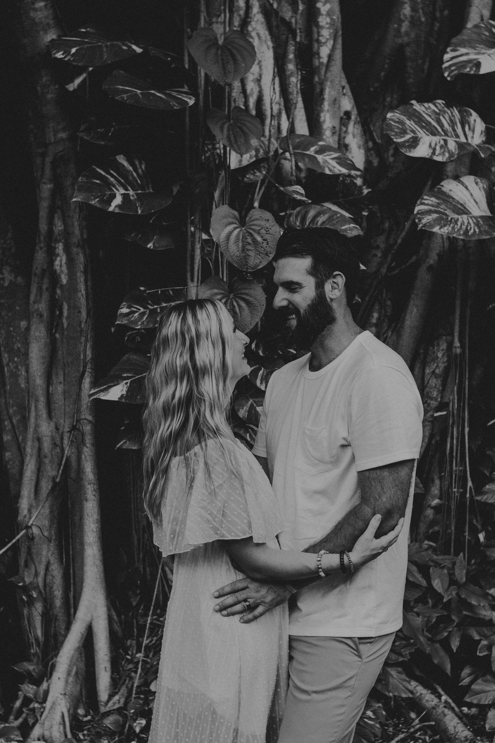 A couple embraces in a romantic black and white photoshoot among tropical foliage and trees.