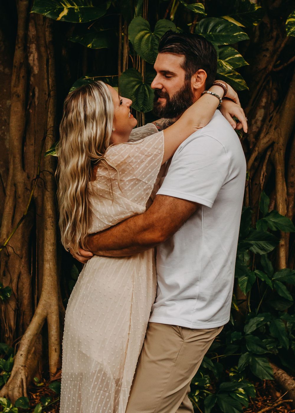 A couple shares an intimate embrace in a lush garden setting with tropical foliage in the background.