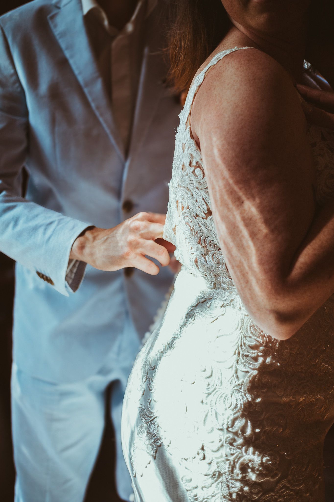 Closeup of groom helping bride button up with her lace wedding dress.