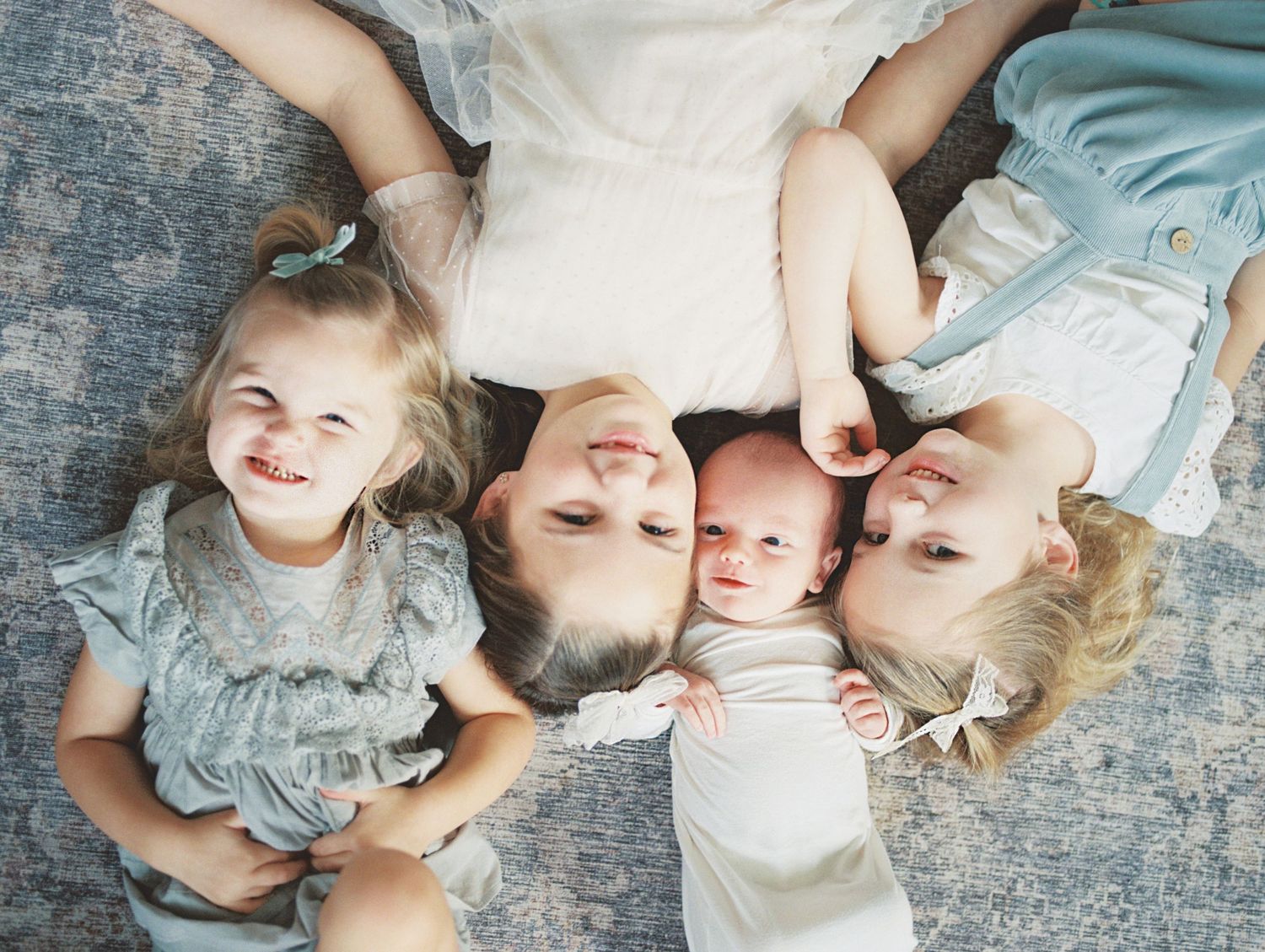 Family members lying on a textured gray surface in a circle formation wearing light blue and white clothing.