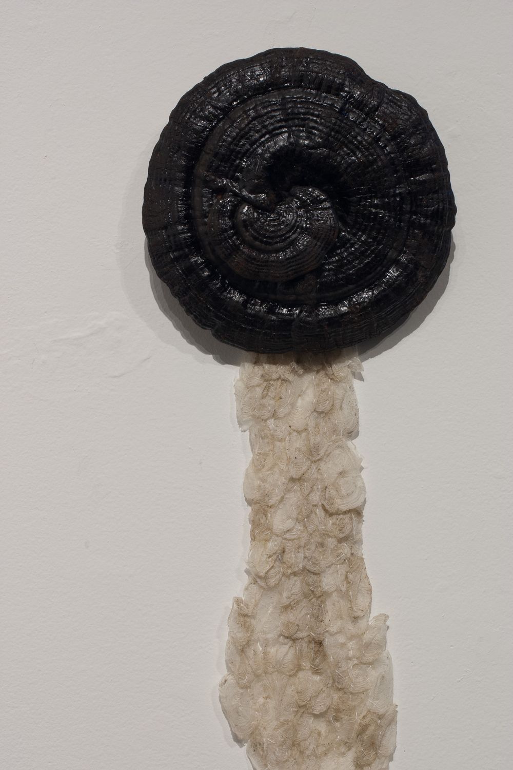 Sculpture resembling a mushroom with black cap and textured pale stem against white background.
