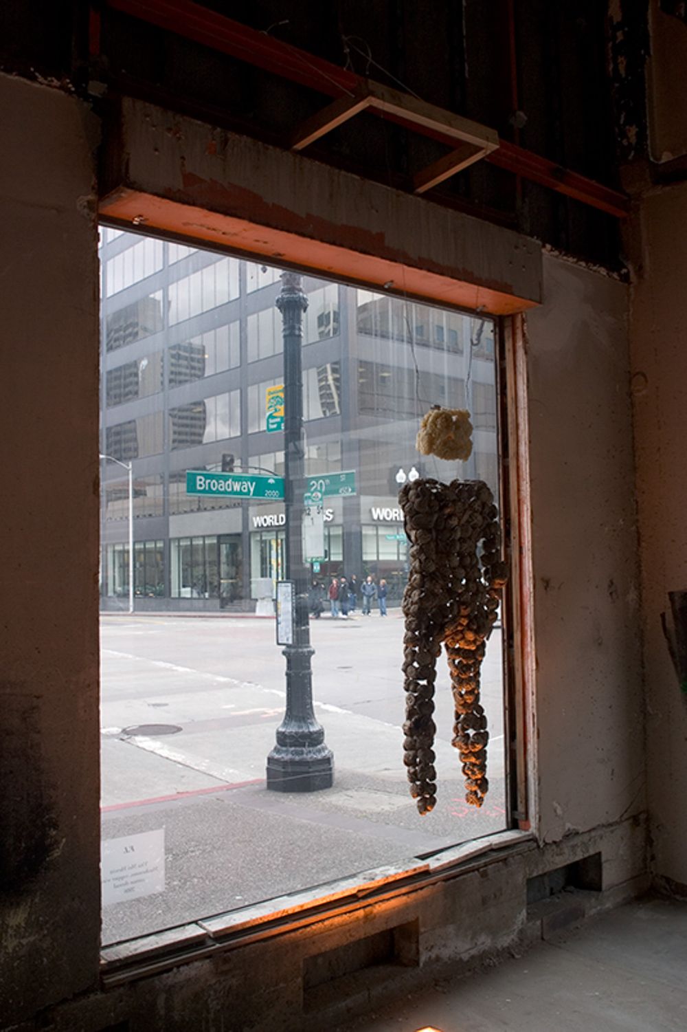 Urban window view of Broadway street with a decorative figure hanging in the frame.