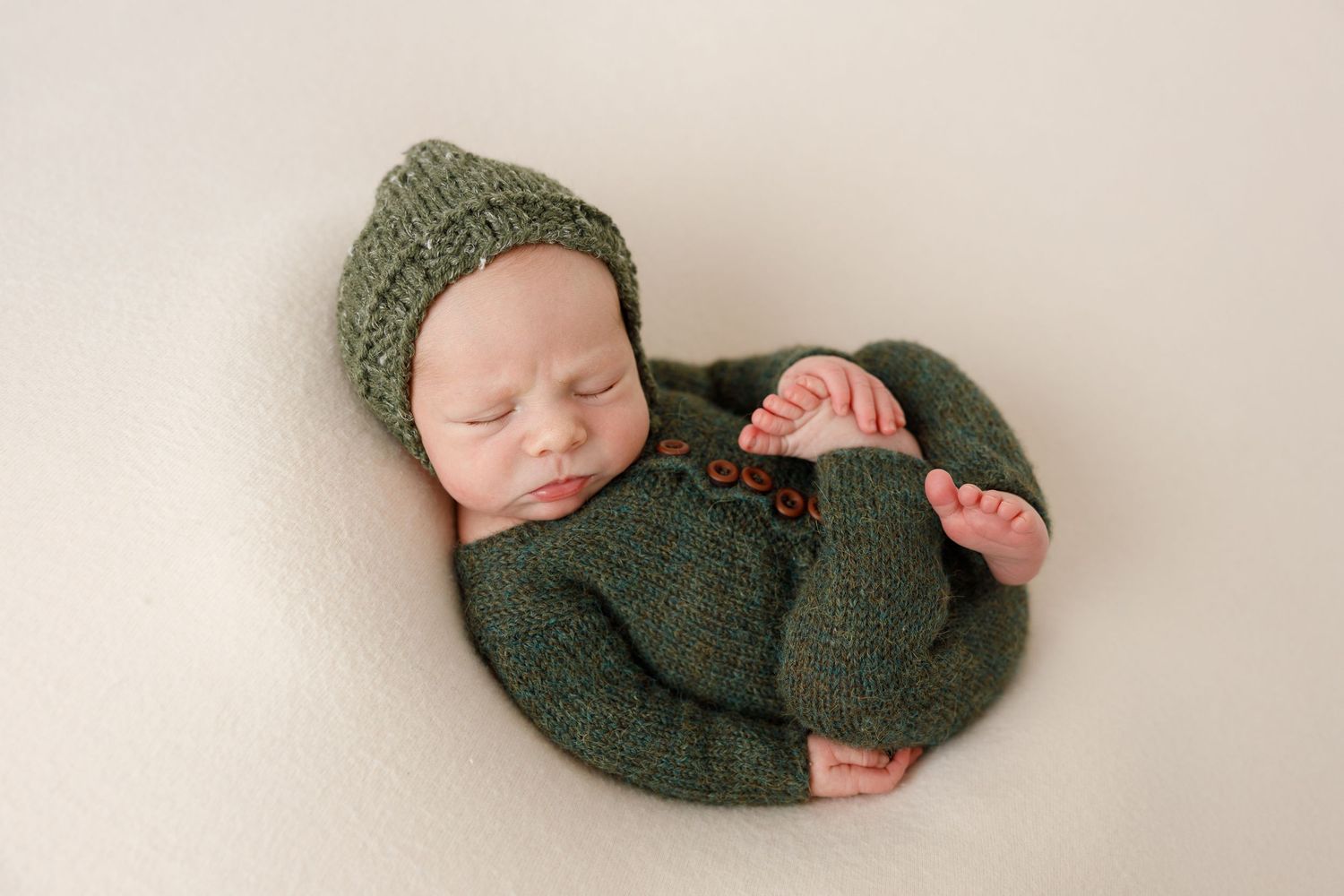 Sleeping newborn baby wearing cozy green knit outfit during studio photography session.