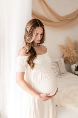 Soft white maternity photography session with ethereal lighting and neutral tones.