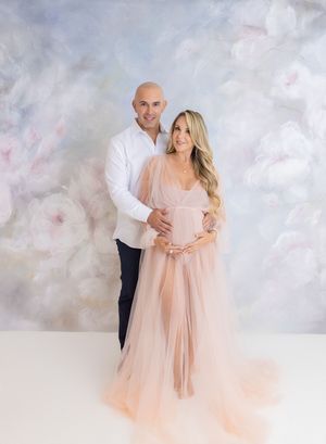 Romantic maternity session with flowing blush gown against painted backdrop.