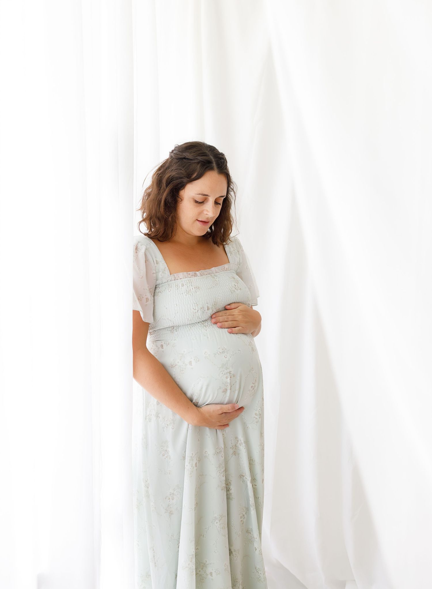 Maternity studio portraits in soft mint green dress against white backdrop.