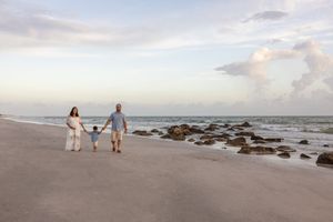 Family maternity beach session with soft pastel sky and rocky coastline.
