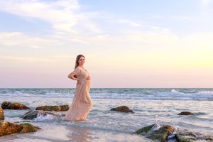 Romantic beach maternity session with soft waves and rocks during golden hour sunset.