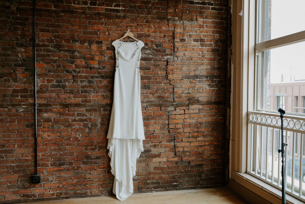 White wedding dress hanging in front of exposed brick wall with natural light.