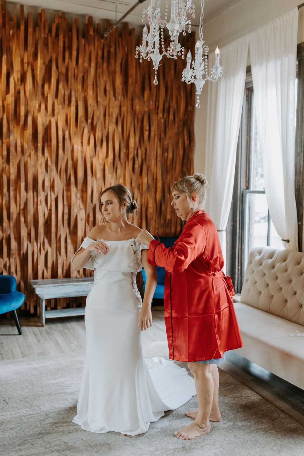 Wedding dress preparations in an elegant room with wooden accent walls and crystal chandelier.