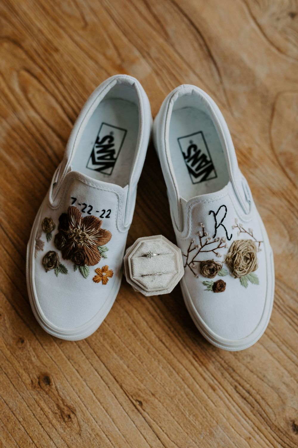 White decorated wedding shoes with floral accents displayed on wooden surface.