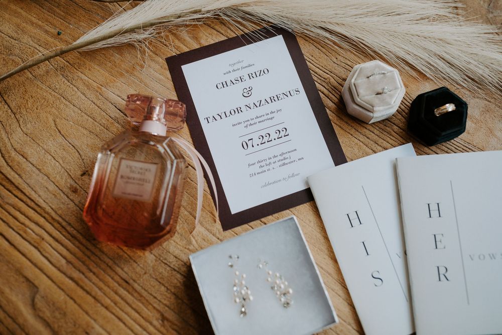 Wedding details including invitations and jewelry arranged on wooden surface.