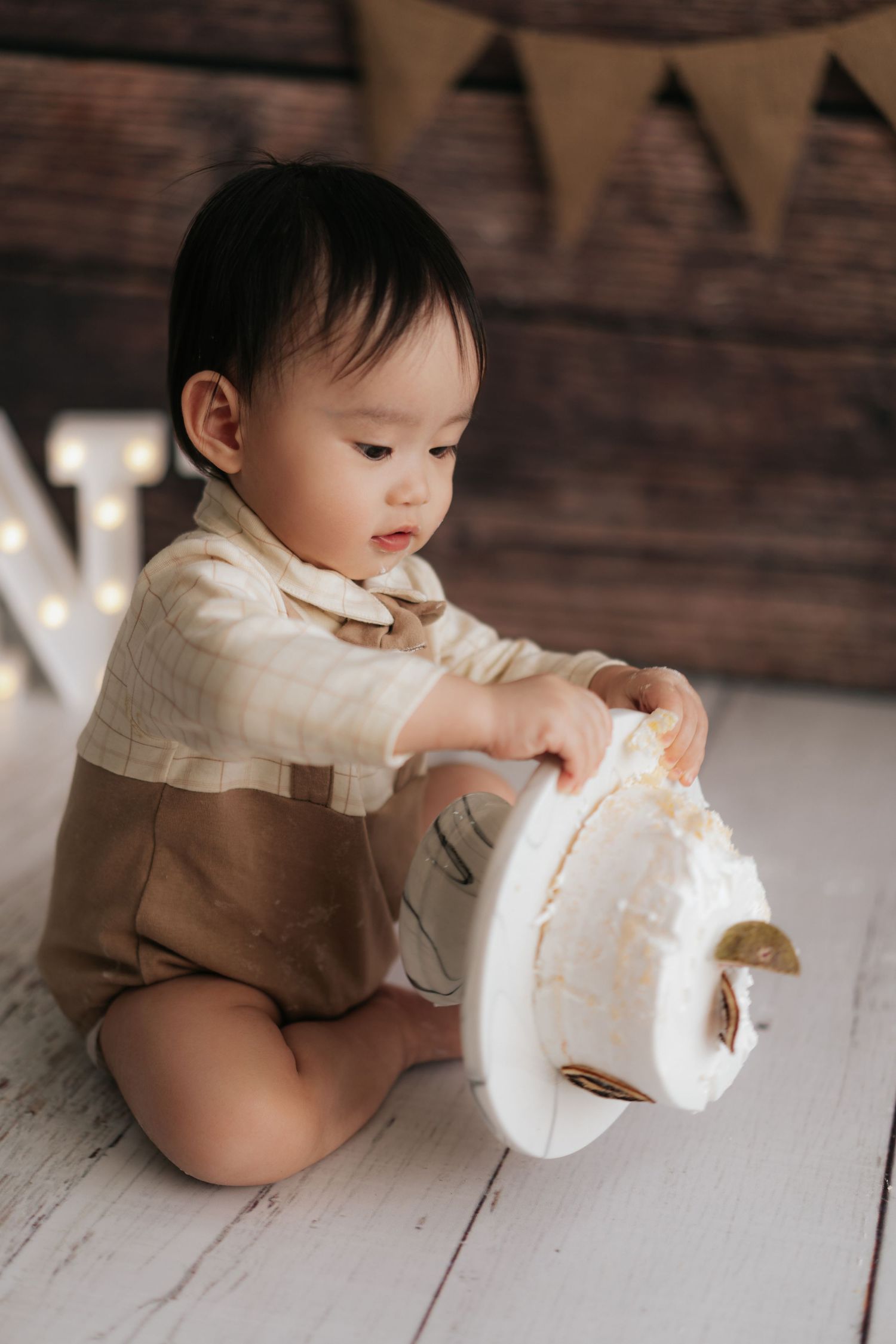 Baby in white and brown outfit sits on wooden floor examining a white plush toy.