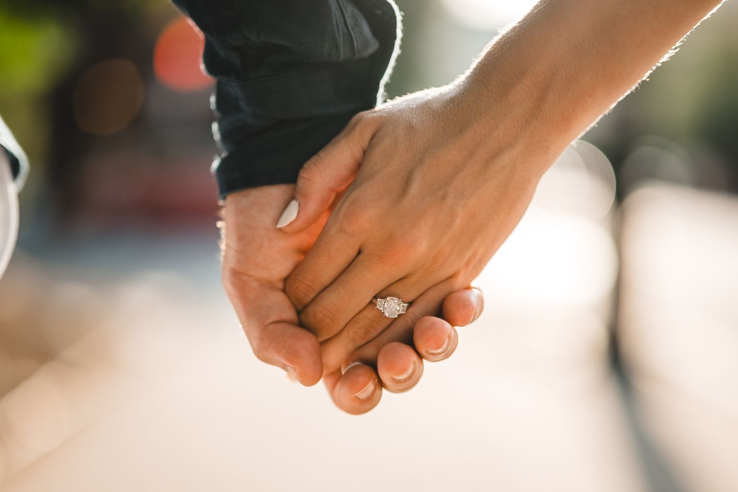 Close-up of engaged couple's hands with diamond ring sparkling in sunlight.