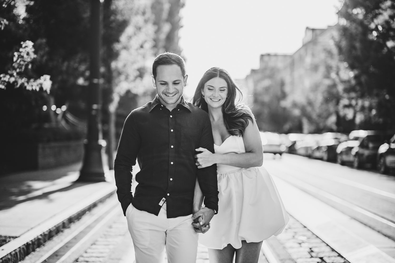 Black and white portrait on tree-lined street with urban backdrop.