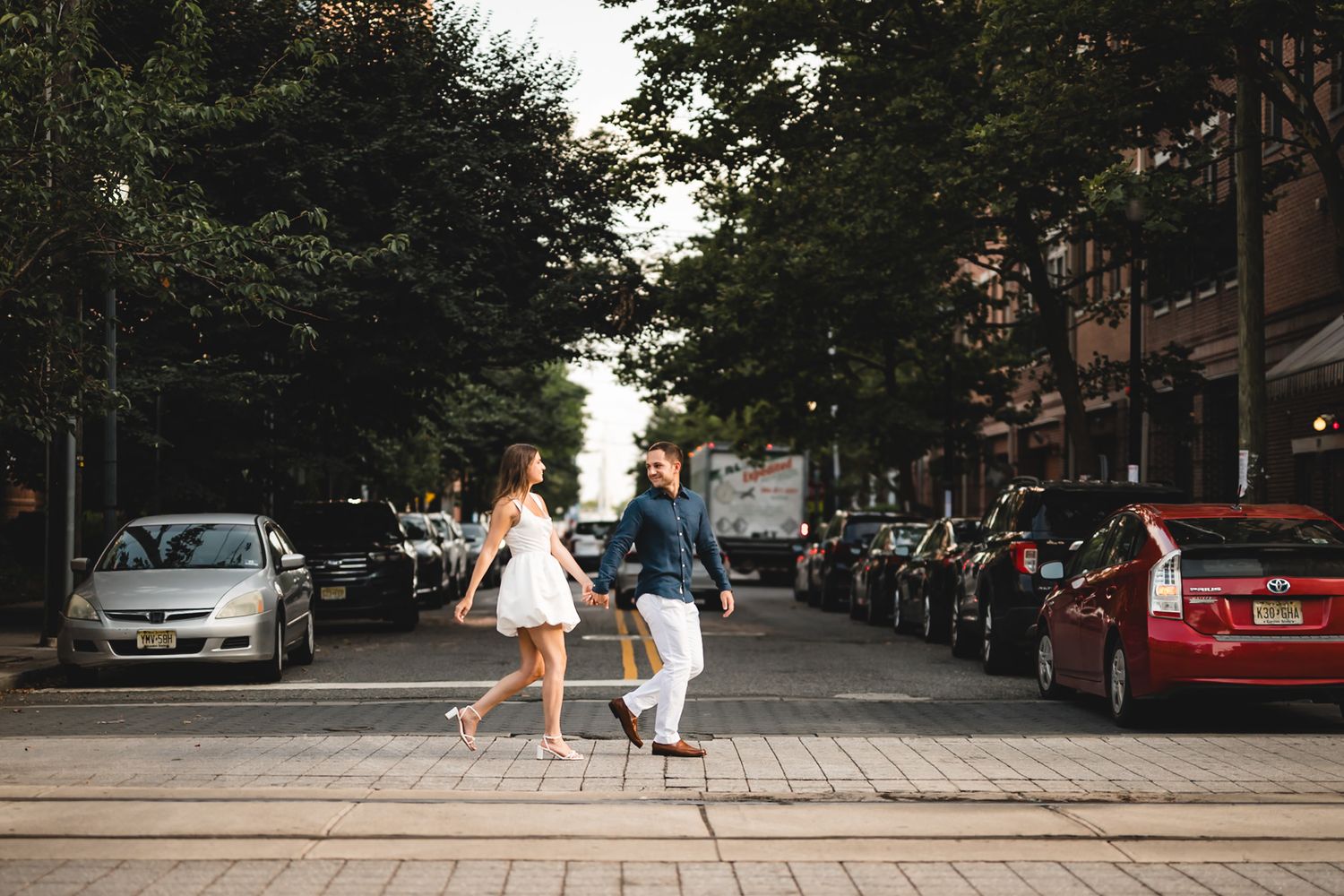 Romantic dance sequence on an urban street with trees and parked cars in the background.