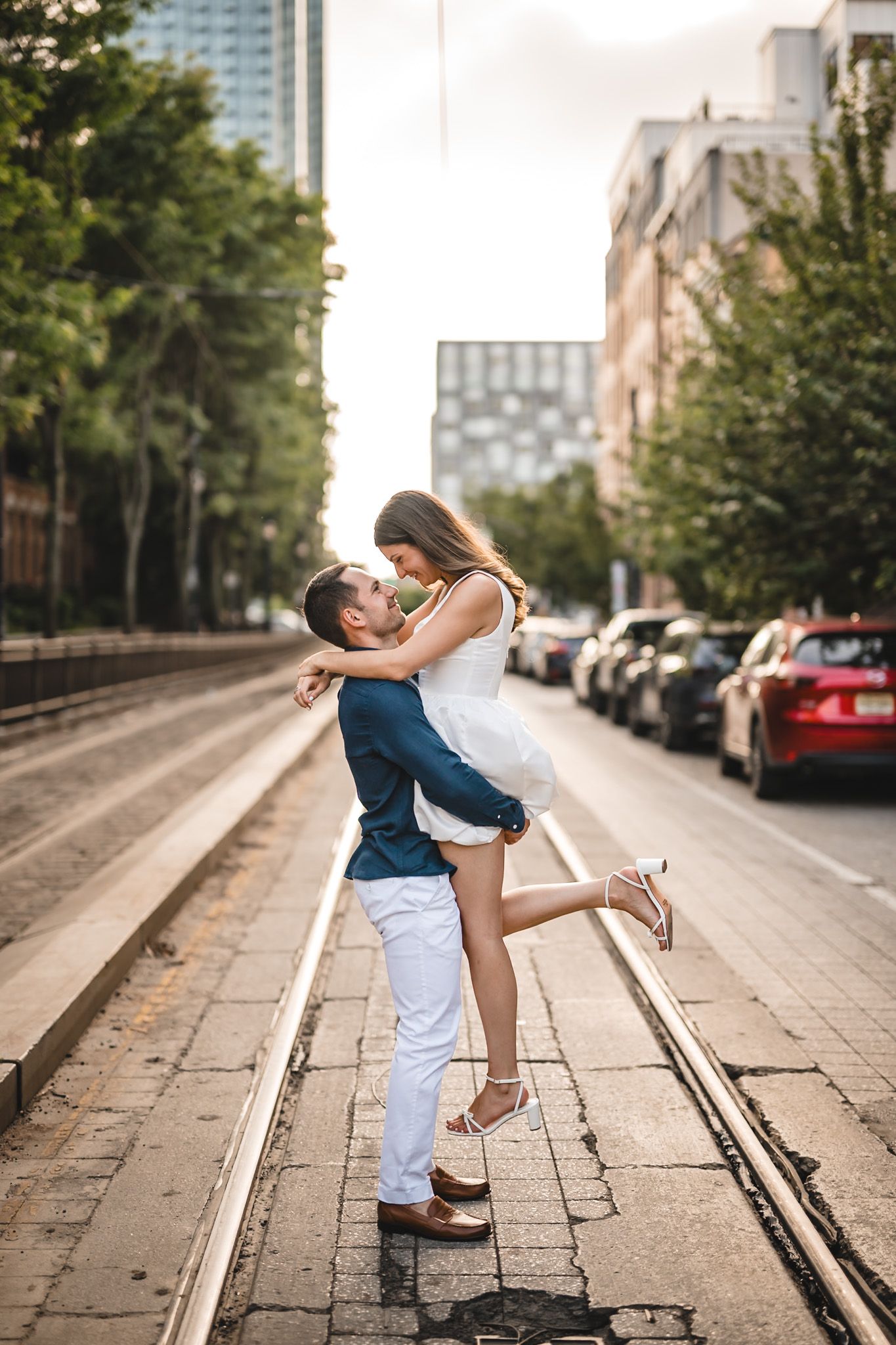 Couple in white and navy outfits dancing playfully on a city sidewalk with brick buildings in the background.