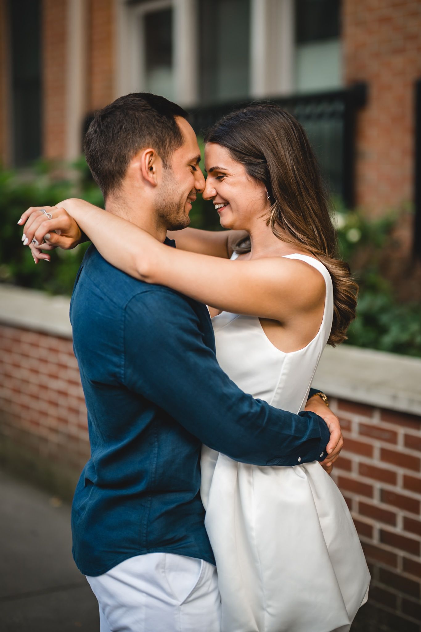 Intimate moment captured between couple embracing against brick wall background.