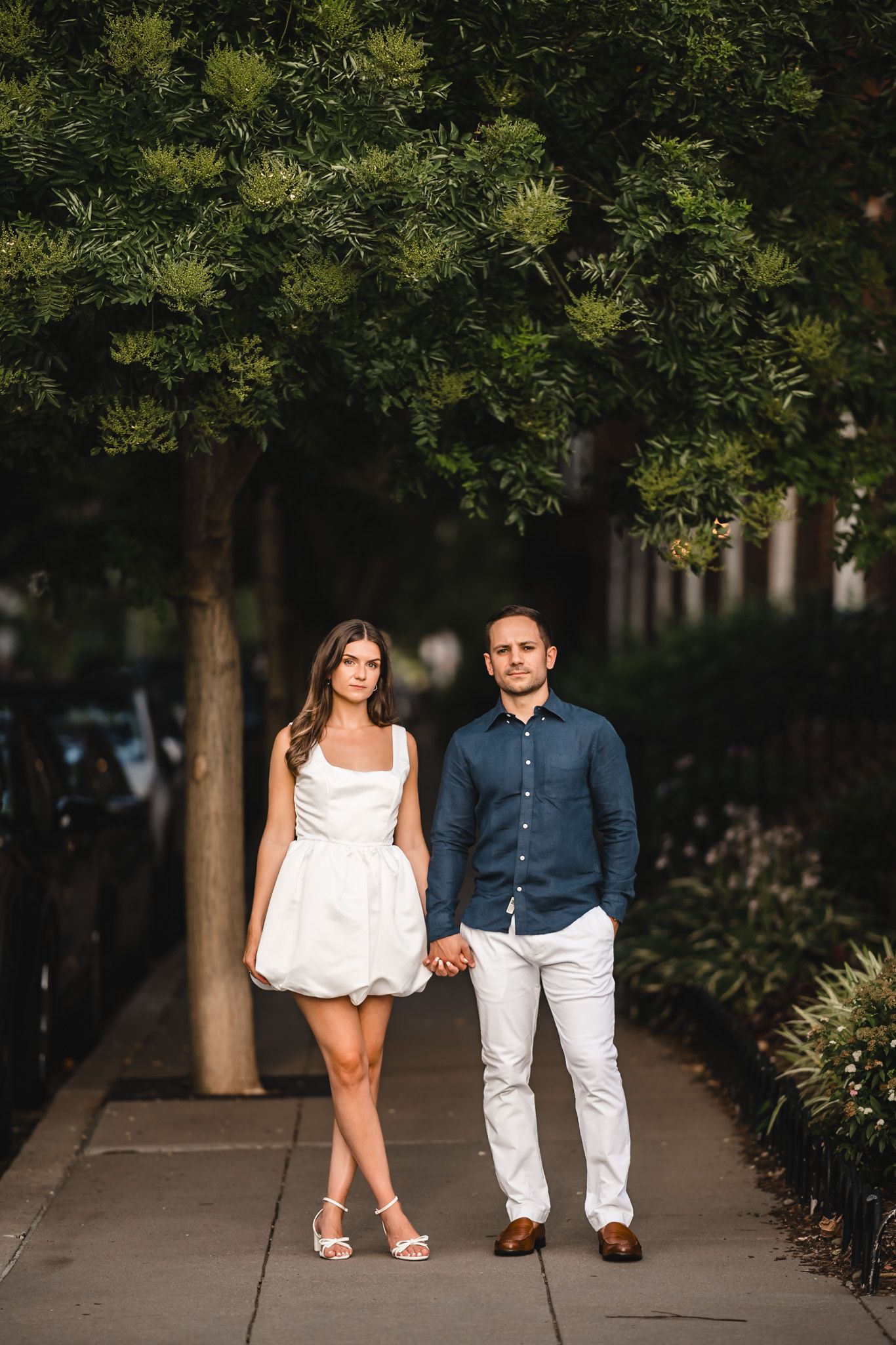 Couple in coordinated navy and white outfits walking along tree-lined urban pathway.