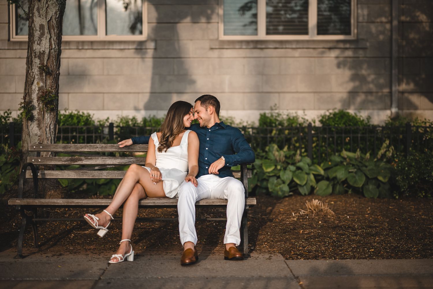 Romantic couple poses on ground against brick wall in urban setting.