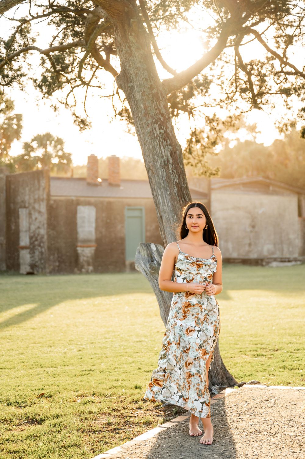 Outdoor portrait session featuring floral dress and natural lighting with trees in background.