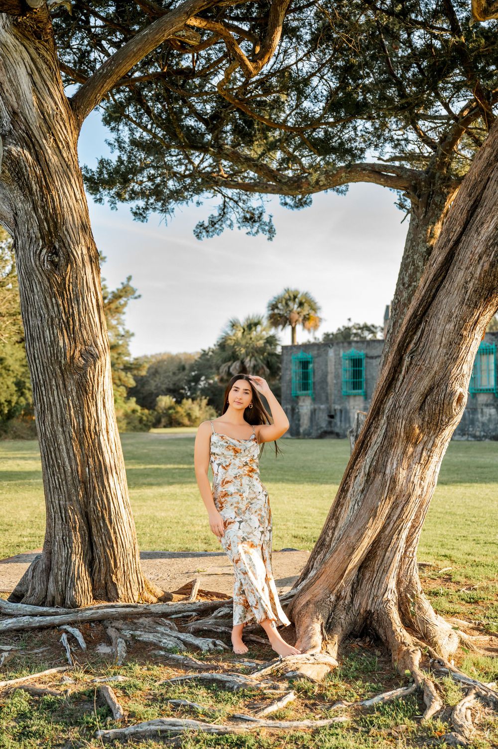 Portrait session under large twisted tree trunks with historic building visible in background.