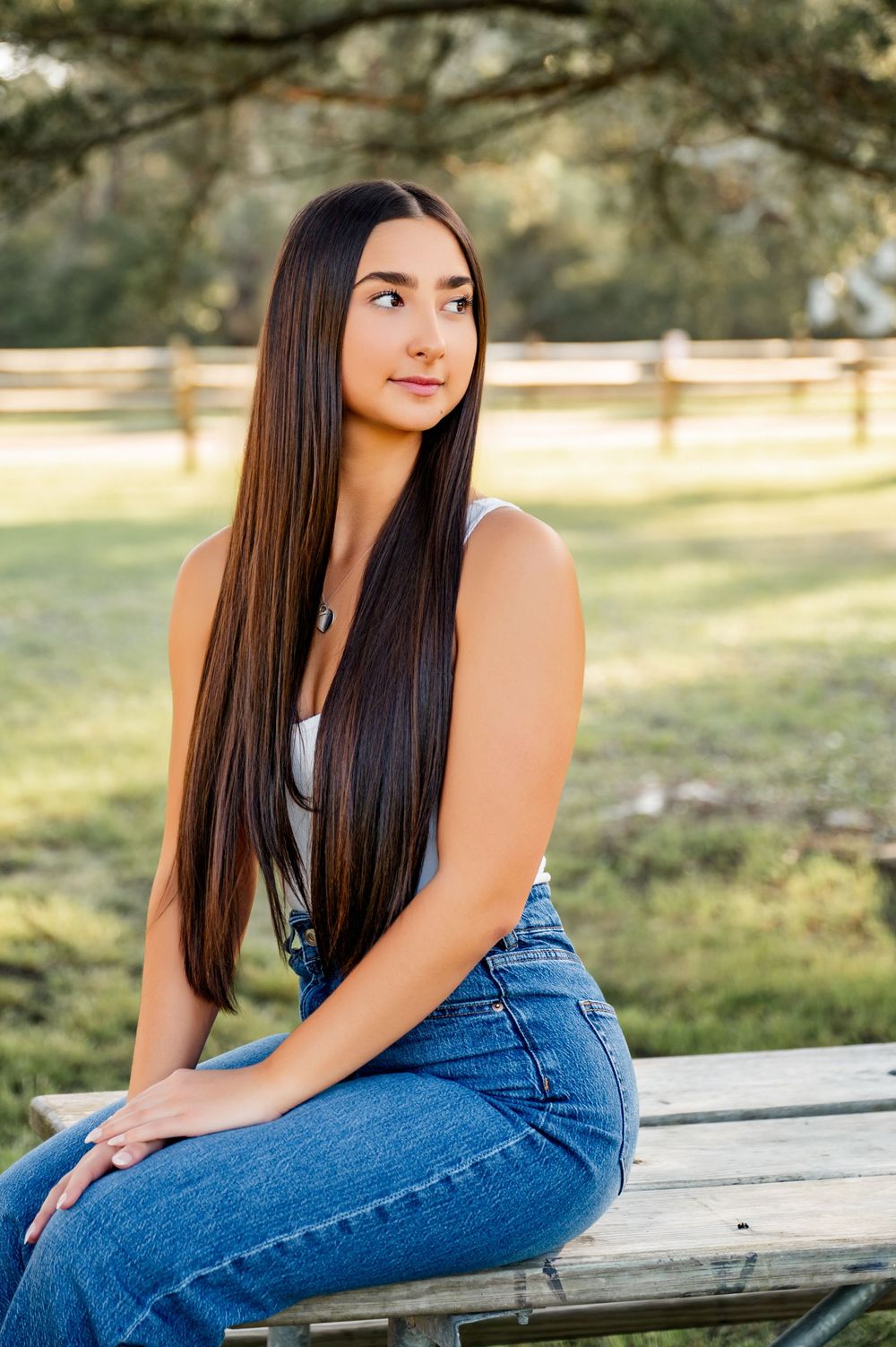 Young woman in casual denim poses on wooden bench during golden hour photoshoot.