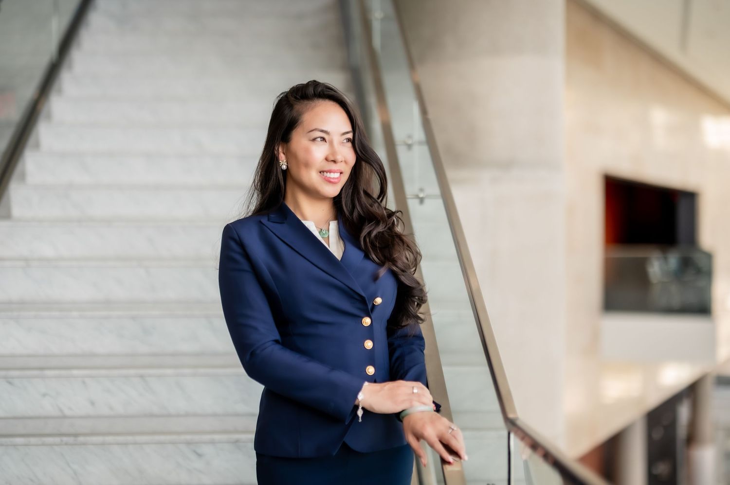 Professional portrait session featuring someone in a navy blue blazer posing against a light architectural background.