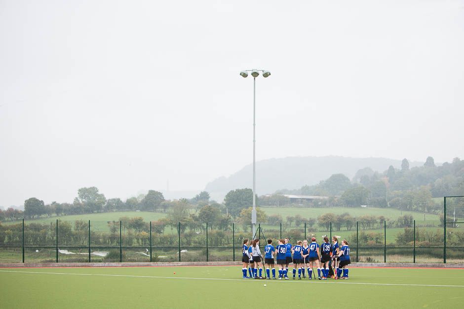 Girls hockey team gathered in huddle before match on outdoor pitch in Gloucestershire