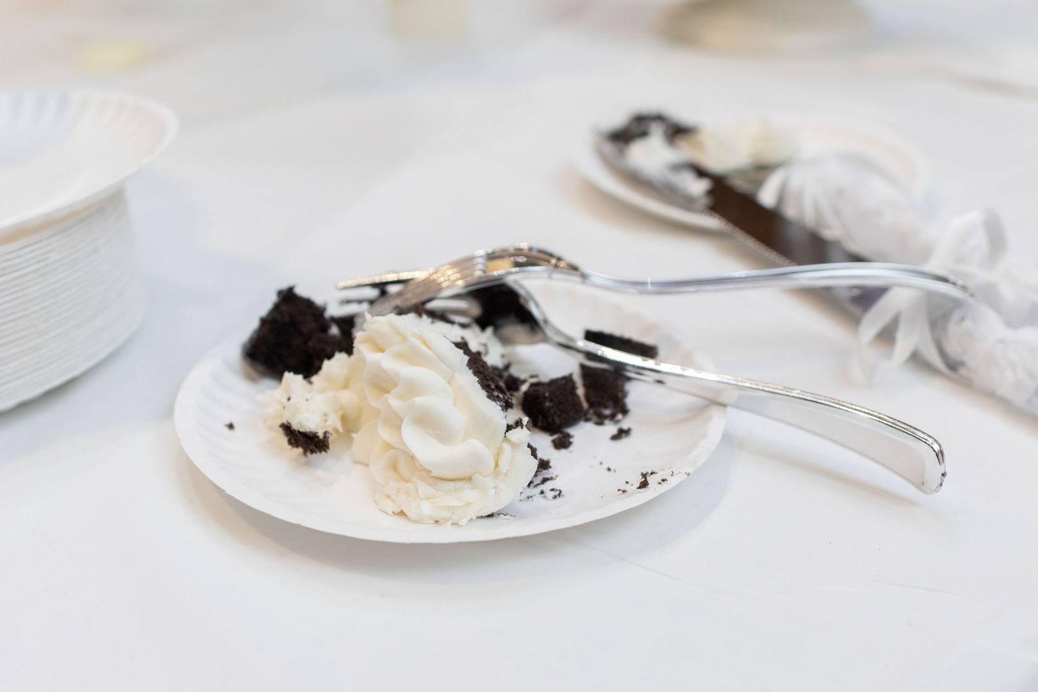 Creamy chocolate wedding cake topped with luxurious white frosting served on a white plate with a silver spoon.